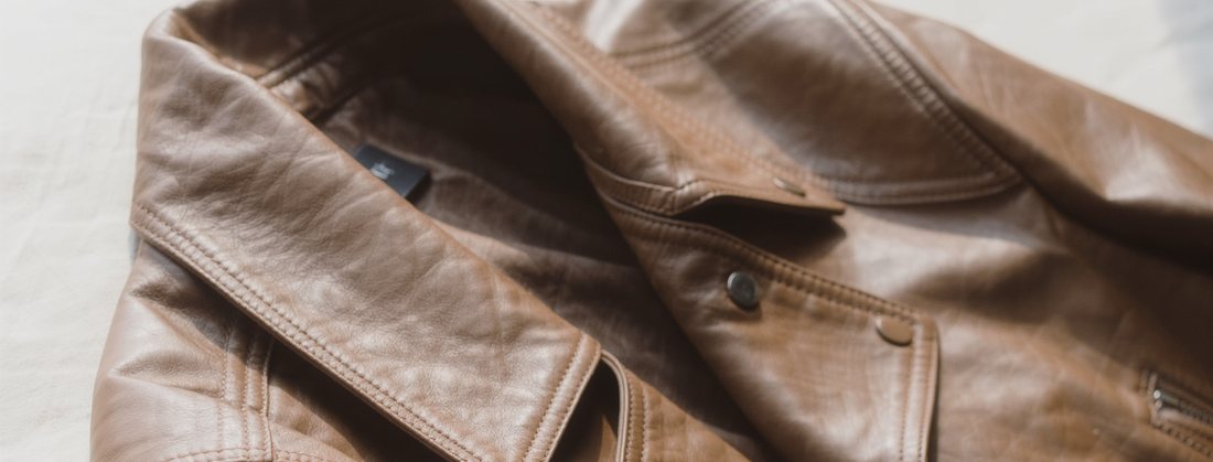 A tan leather jacket laid flat on linen, collar and zip in soft light.